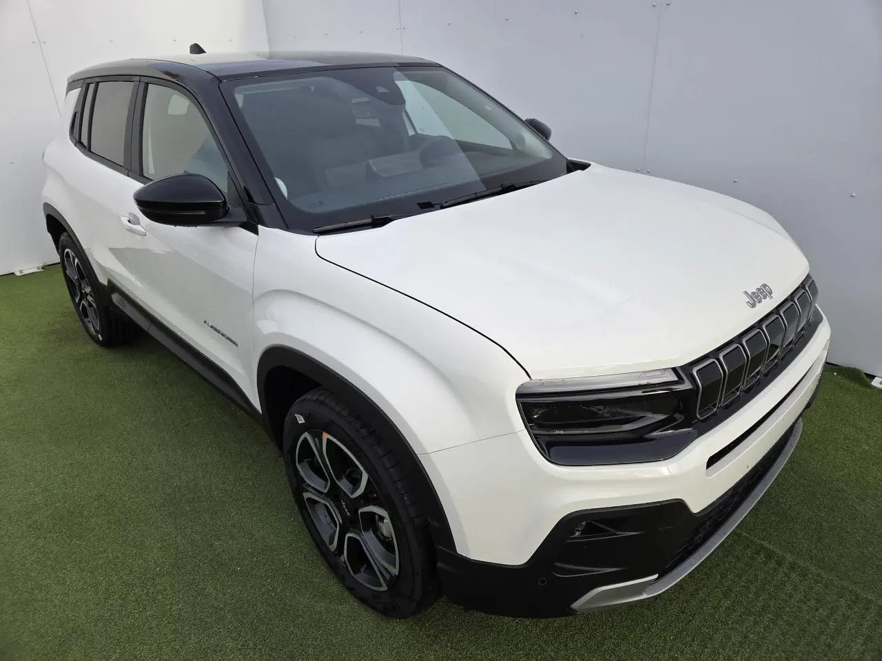 Jeep Avenger blanc Snow avec toit noir Volcano, vue 3/4 avant droit mettant en valeur la calandre gloss black.