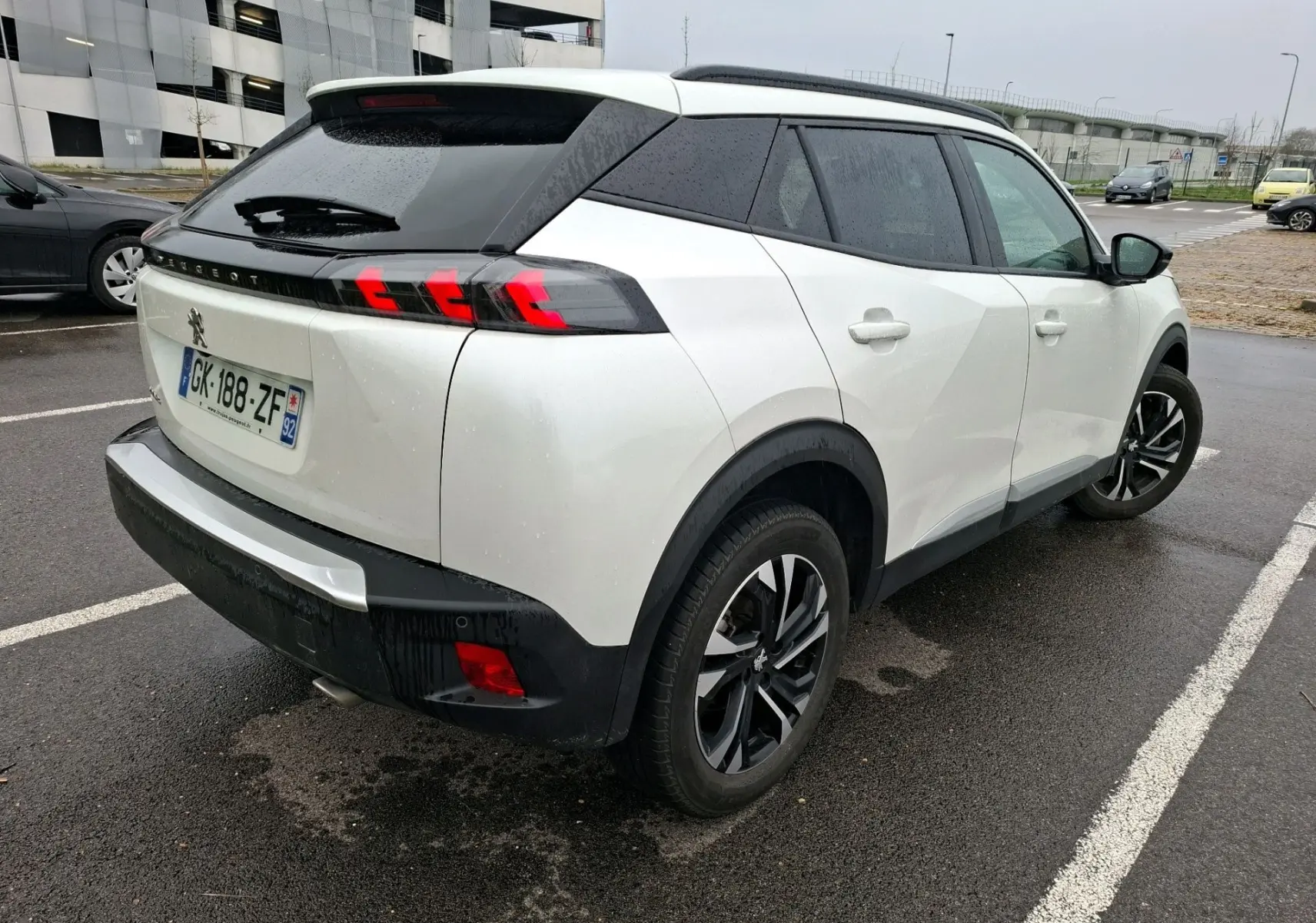 Vue 3/4 arrière droite d’un Peugeot 2008 blanc nacré avec feux arrière à griffes rouges et jantes noires.