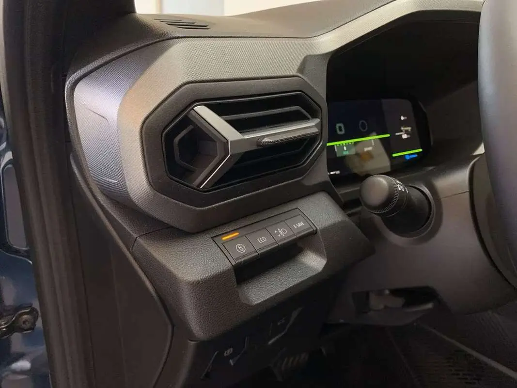 Détail intérieur côté gauche du tableau de bord bleu indigo du Dacia Bigster Hybrid avec commandes et aérateur hexagonal.