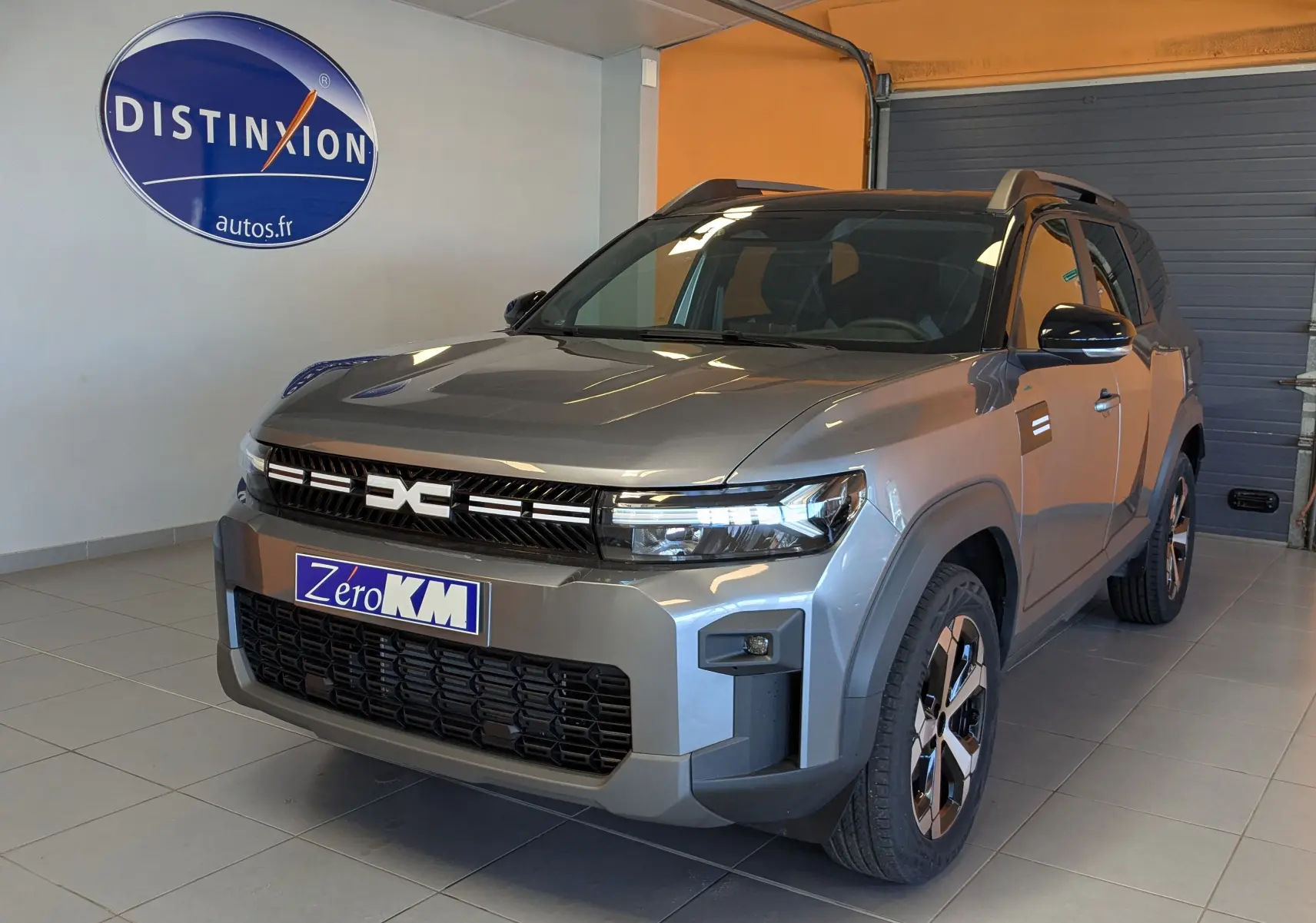 Vue 3/4 avant d'un Dacia Bigster Hybrid 155 gris schiste avec jantes alliage et toit bi-ton noir en intérieur showroom.