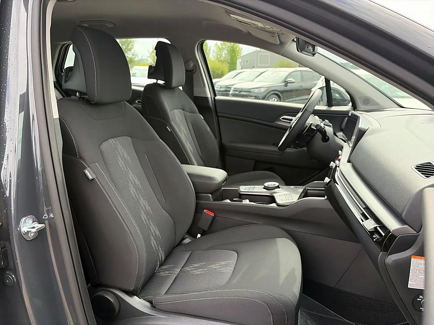 Vue intérieure côté conducteur du Kia Sportage 1.6 hybride 239 gris eclipse, avec sièges noirs et console centrale moderne.