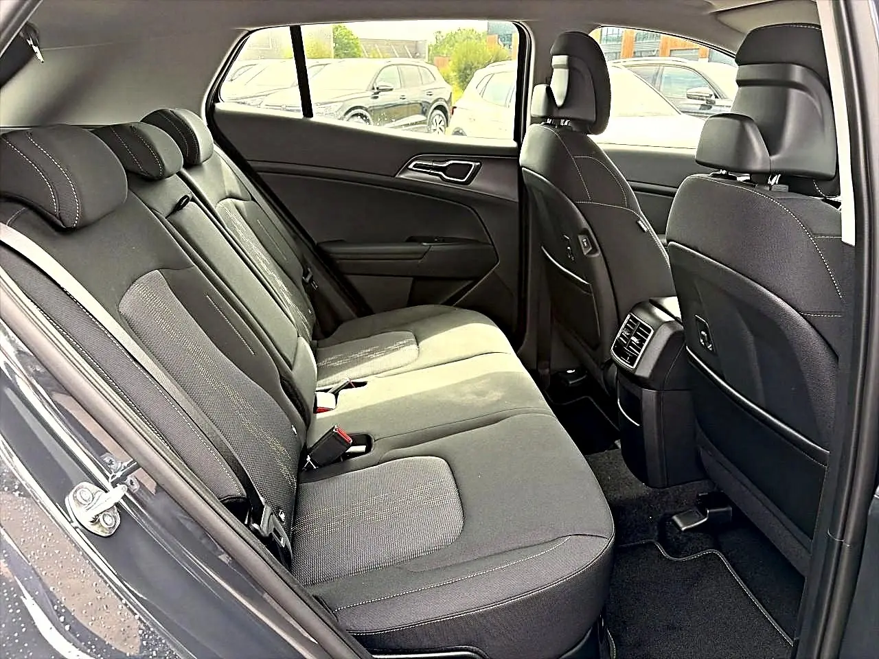 Vue intérieure côté gauche montrant la banquette arrière grise et les sièges avant du Kia Sportage 1.6 hybride 2026.