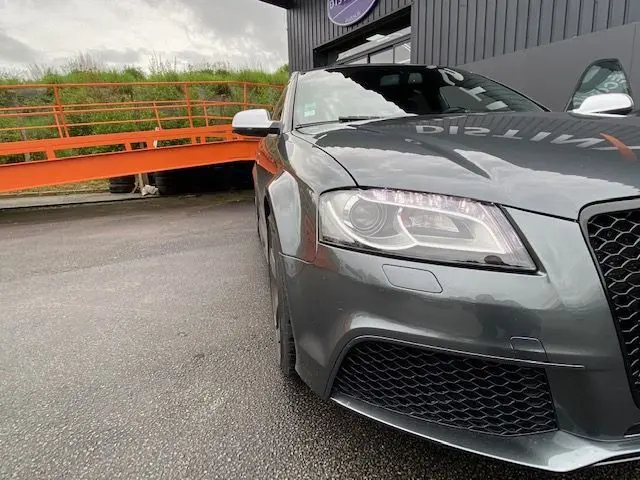 Gros plan sur l'avant droit de l'Audi RS3 Sportback gris Daytona, mettant en valeur ses phares LED et sa calandre noire.