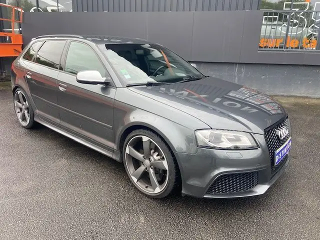 Audi RS3 Sportback gris Daytona vue 3/4 avant droit, avec jantes alliage 5 branches et calandre noire sportive.