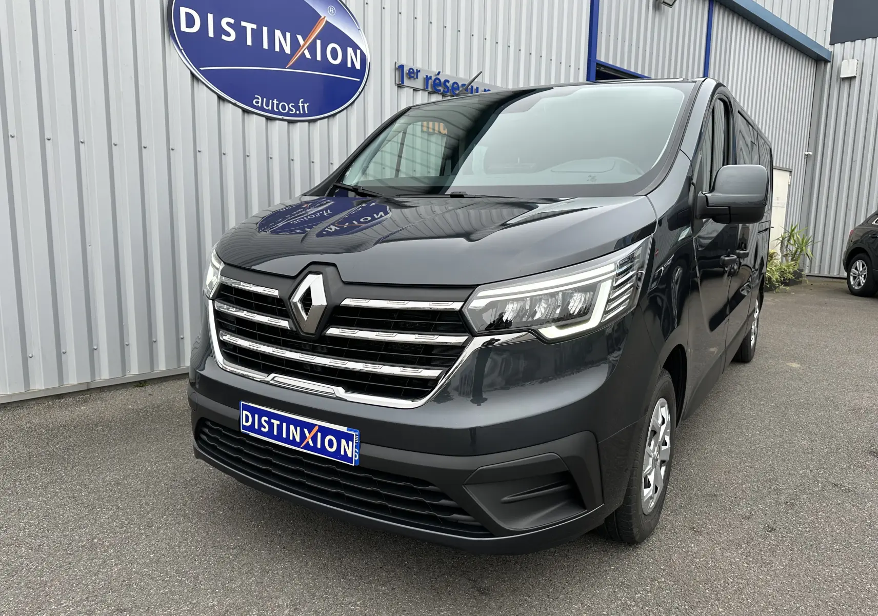Renault Trafic Combi gris Comète en 3/4 avant droit, avec calandre chromée et phares LED allumés.