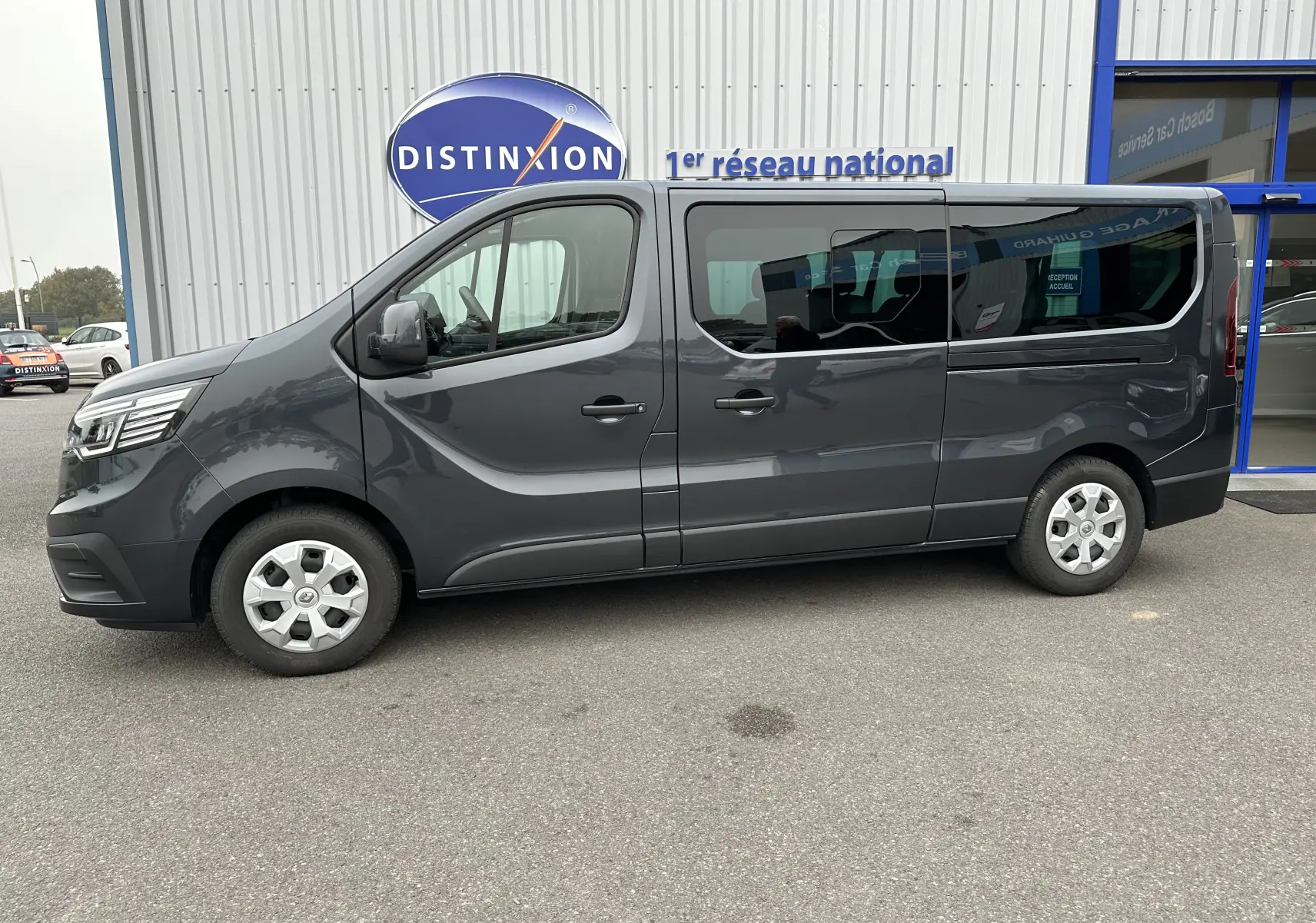 Profil côté gauche d'un Renault Trafic Combi gris comète 2023, véhicule utilitaire long avec vitres teintées.