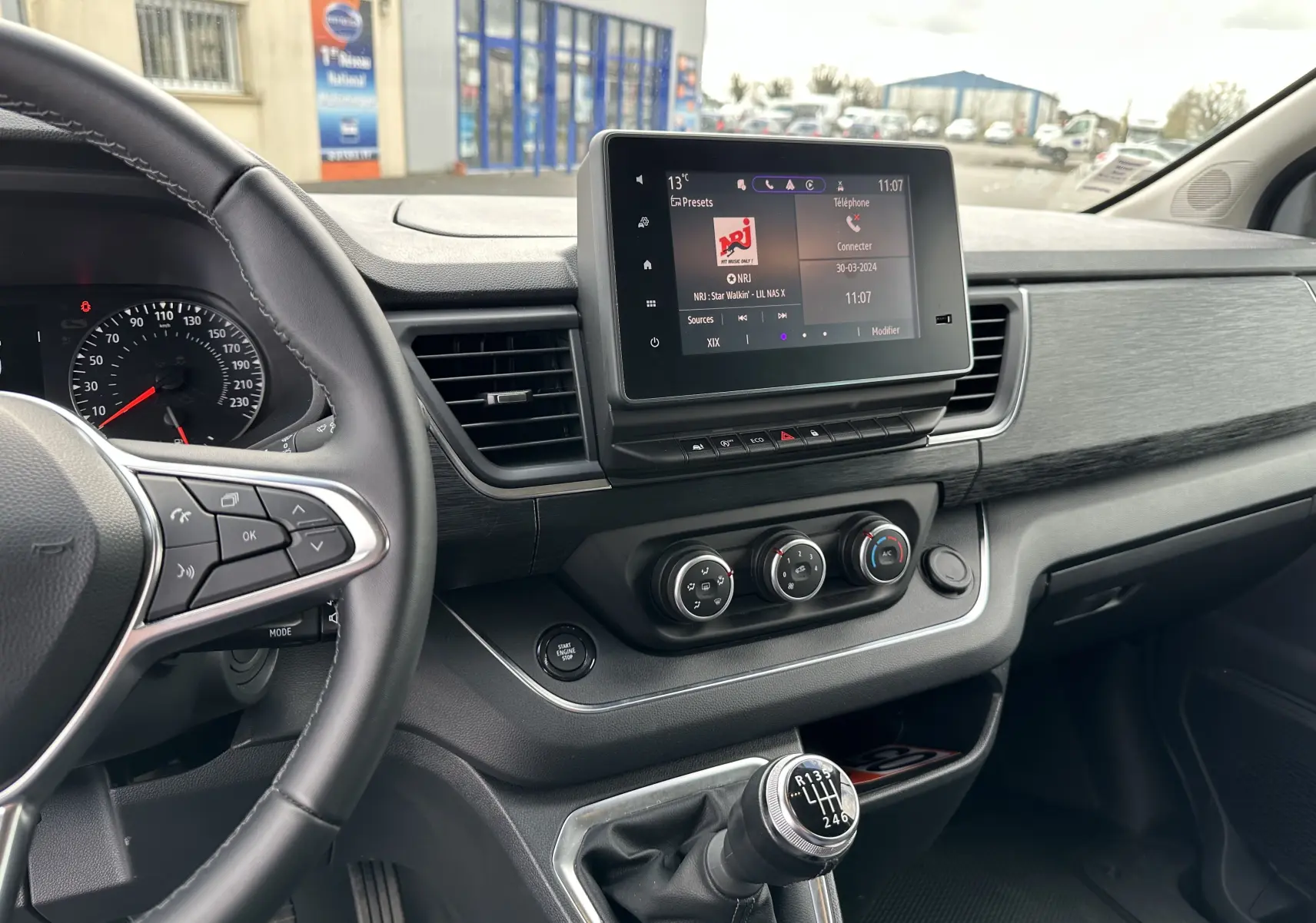 Vue intérieure du tableau de bord et levier de vitesses manuel du Renault Trafic Combi gris comète 2023, avec écran tactile central allumé.