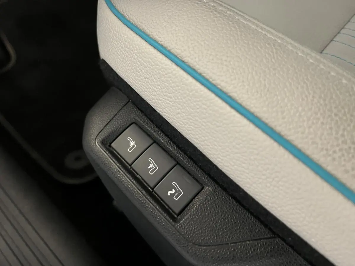 Détail des commandes de réglage électrique sous la sellerie ivoire soft touch avec surpiqûres bleues du Fiat 600 hybride 2024.