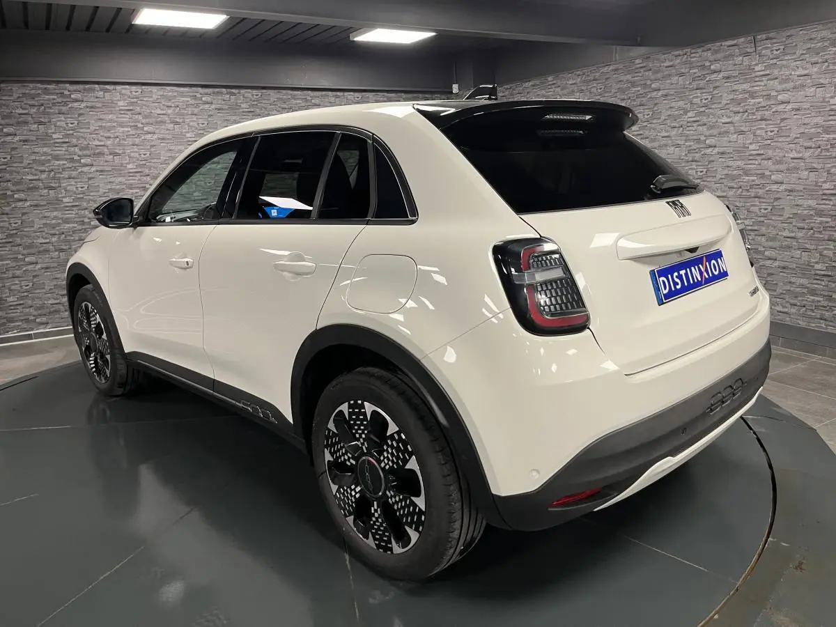 Vue 3/4 arrière droite d'une FIAT 600 blanche avec jantes alliage noires et toit noir brillant en intérieur showroom.