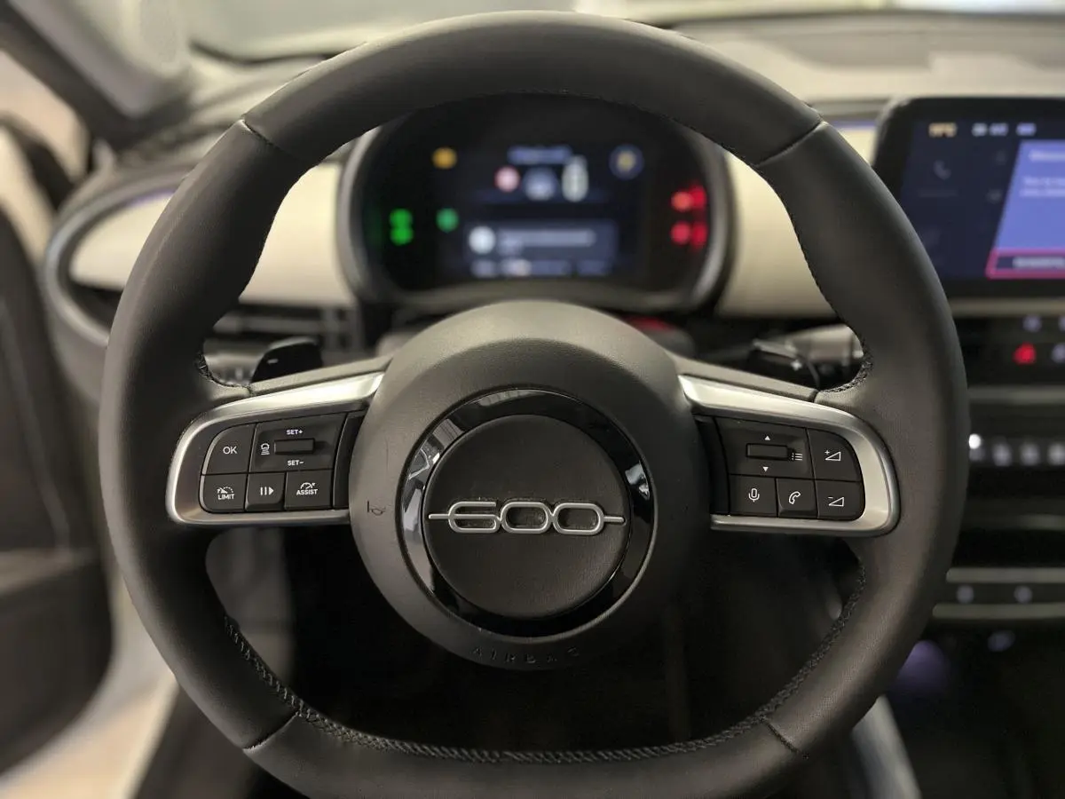 Volant noir avec logo 600 chromé au centre, planche de bord ivoire et écran numérique du Fiat 600 hybride 2024.