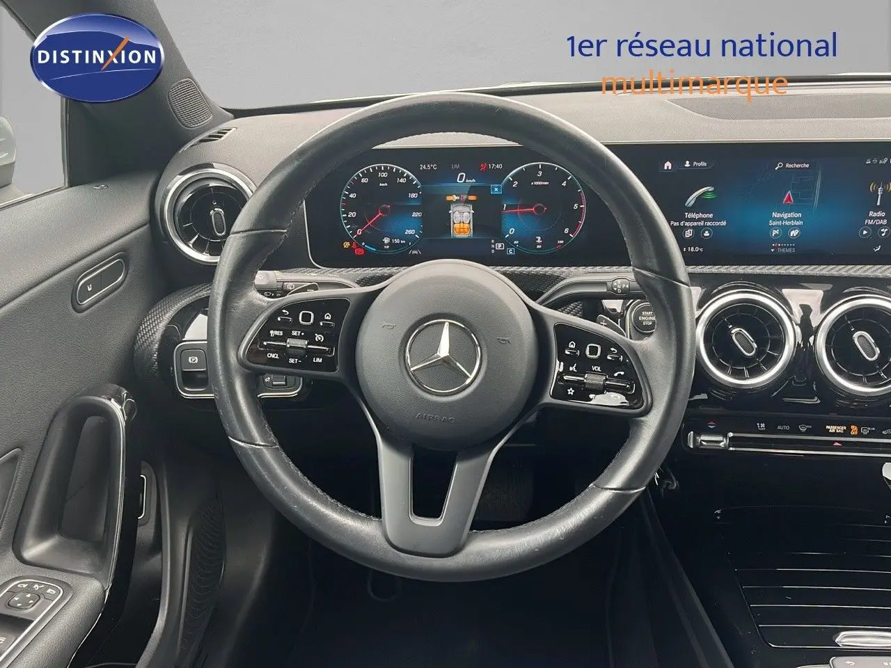 Vue frontale du tableau de bord et du volant en cuir noir d'une Mercedes CLA Shooting Brake 180 argent iridium, avec écran numérique et aérateurs ronds chromés.