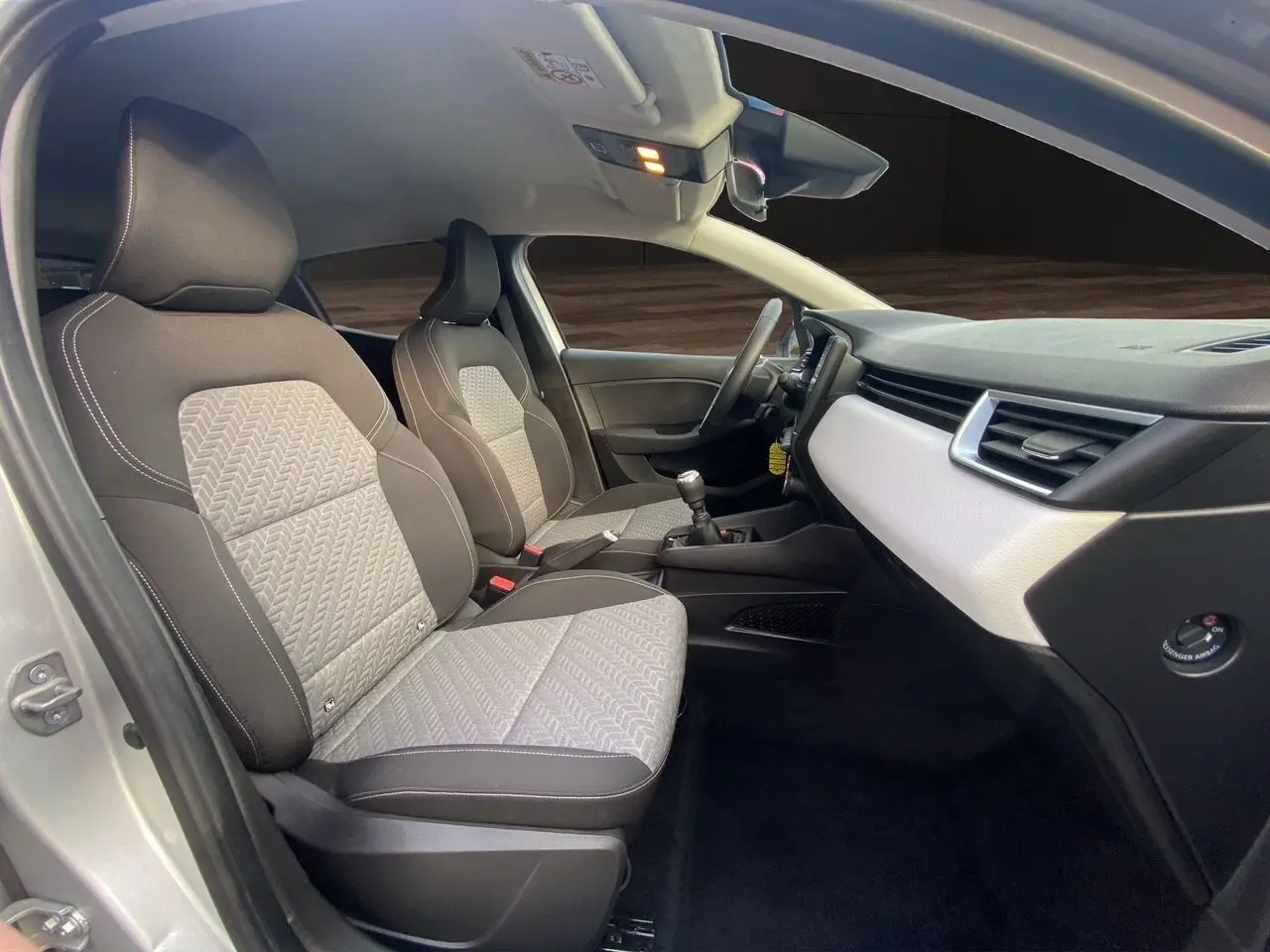 Vue intérieure côté passager de la Renault Clio V 2023 avec sellerie beige et tableau de bord gris clair.