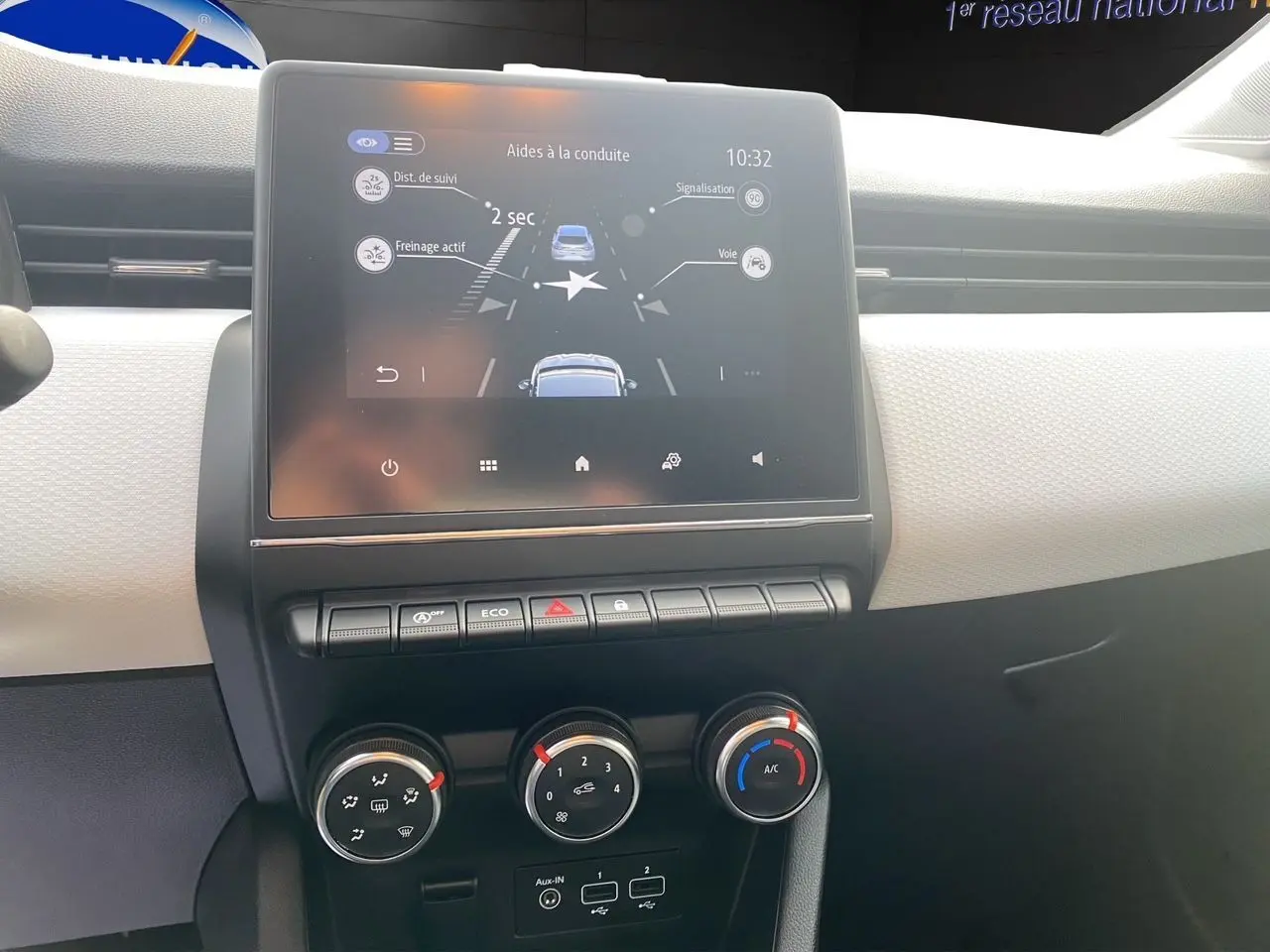 Vue rapprochée du tableau de bord beige de la Renault Clio V avec écran tactile 7 pouces et commandes de climatisation manuelle.