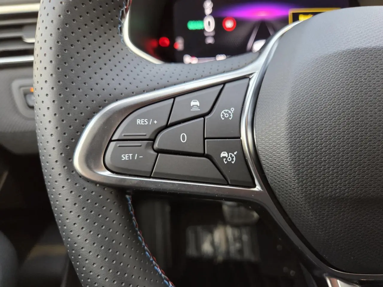 Gros plan sur les commandes du volant perforé noir avec surpiqûres bleues de la Renault Clio V hybride Gris Rafale.