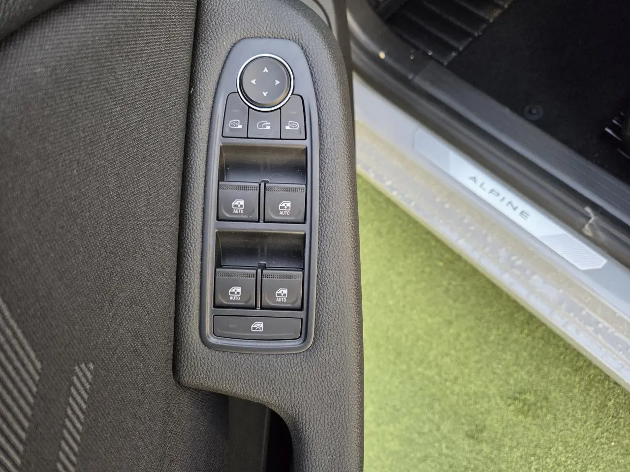 Gros plan sur les commandes des vitres et rétroviseurs côté gauche, seuil de porte Alpine visible sur Renault Clio Gris Rafale.