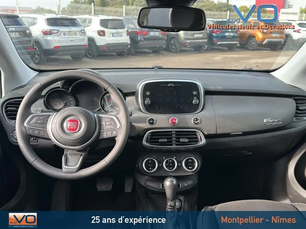 Vue intérieure du tableau de bord et volant du FIAT 500X noir MY23 avec écran tactile central et commandes au volant.