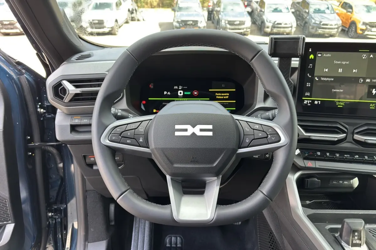 Vue intérieure centrée sur le volant cuir DACIA Bigster Hybrid 155 avec tableau de bord digital et écran tactile.