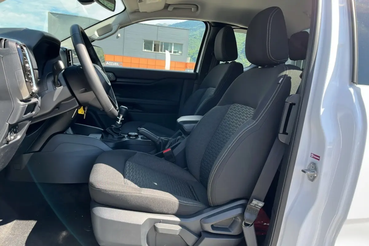 Vue intérieure côté conducteur du Ford Ranger blanc glacier 2025, montrant les sièges noirs et la console centrale avec boîte manuelle.