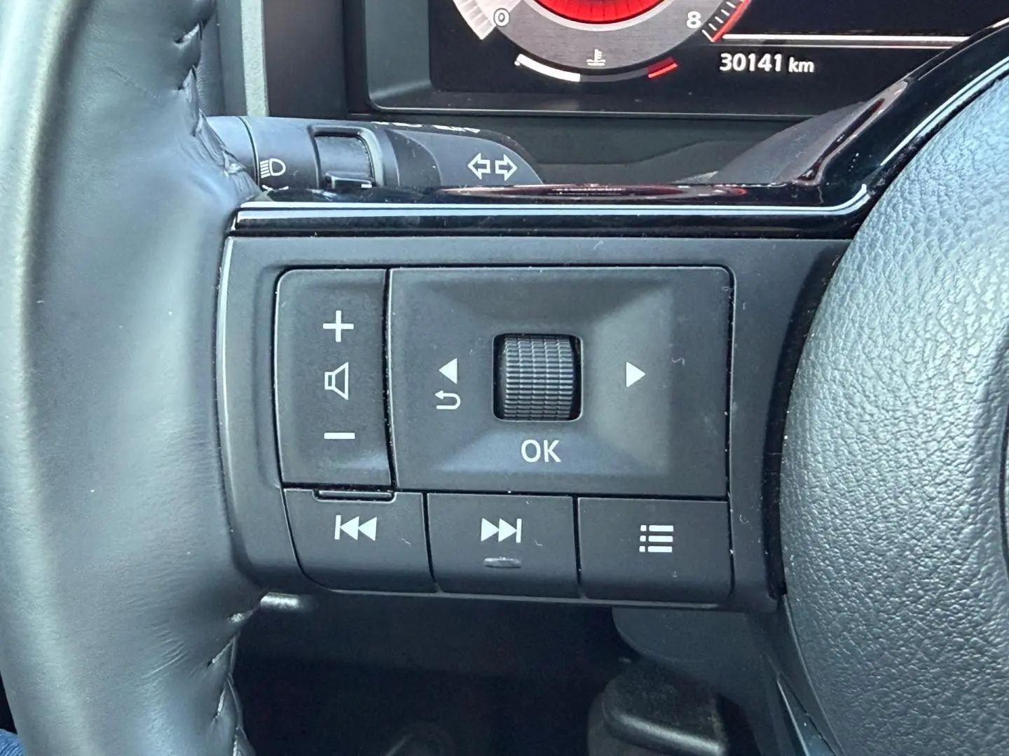 Gros plan sur les commandes multifonctions à gauche du volant cuir du Nissan Qashqai rouge 2022, avec écran numérique partiel visible.