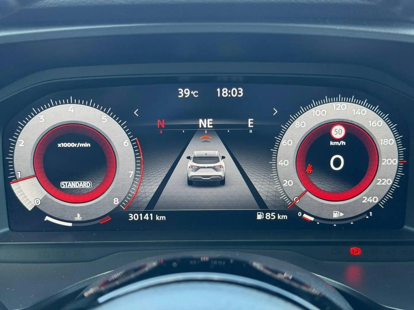 Tableau de bord numérique du Nissan Qashqai 2022 affichant la vitesse, le compte-tours et une vue arrière du véhicule blanc.
