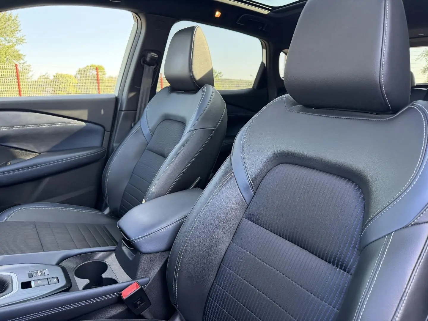 Vue rapprochée des sièges avant en cuir noir du Nissan Qashqai 1.3 Mild Hybrid 2022 avec accoudoir central.