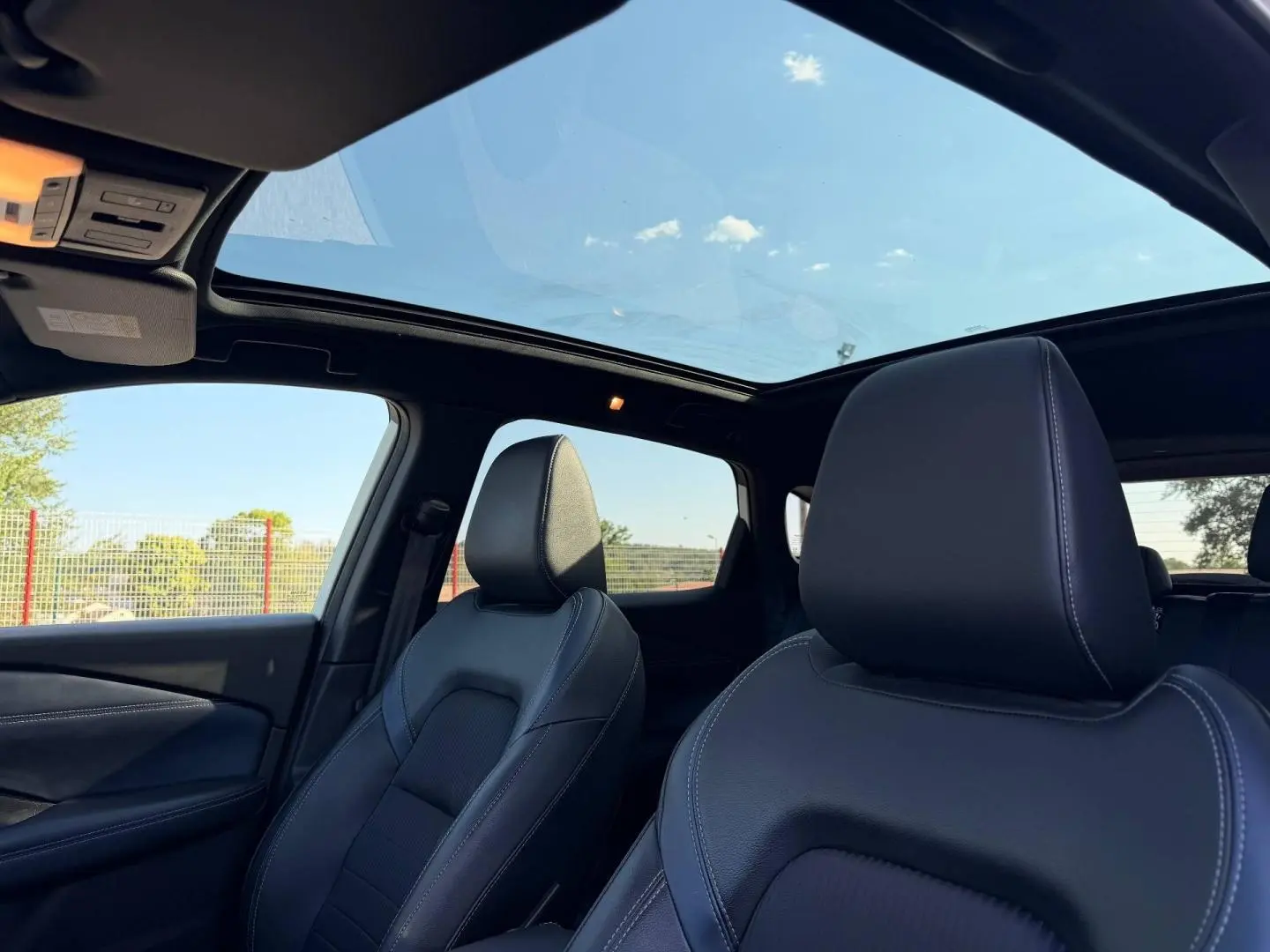 Vue intérieure avant du Nissan Qashqai 2022 avec sièges cuir noirs et toit panoramique ouvrant.