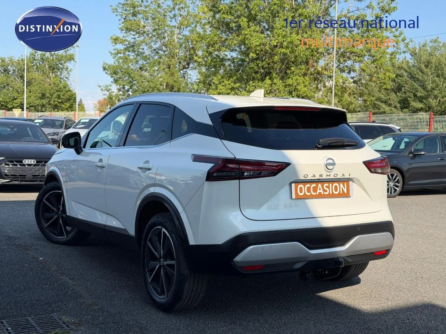 Vue 3/4 arrière gauche d'un Nissan Qashqai blanc avec jantes noires et attelage de remorque visible.