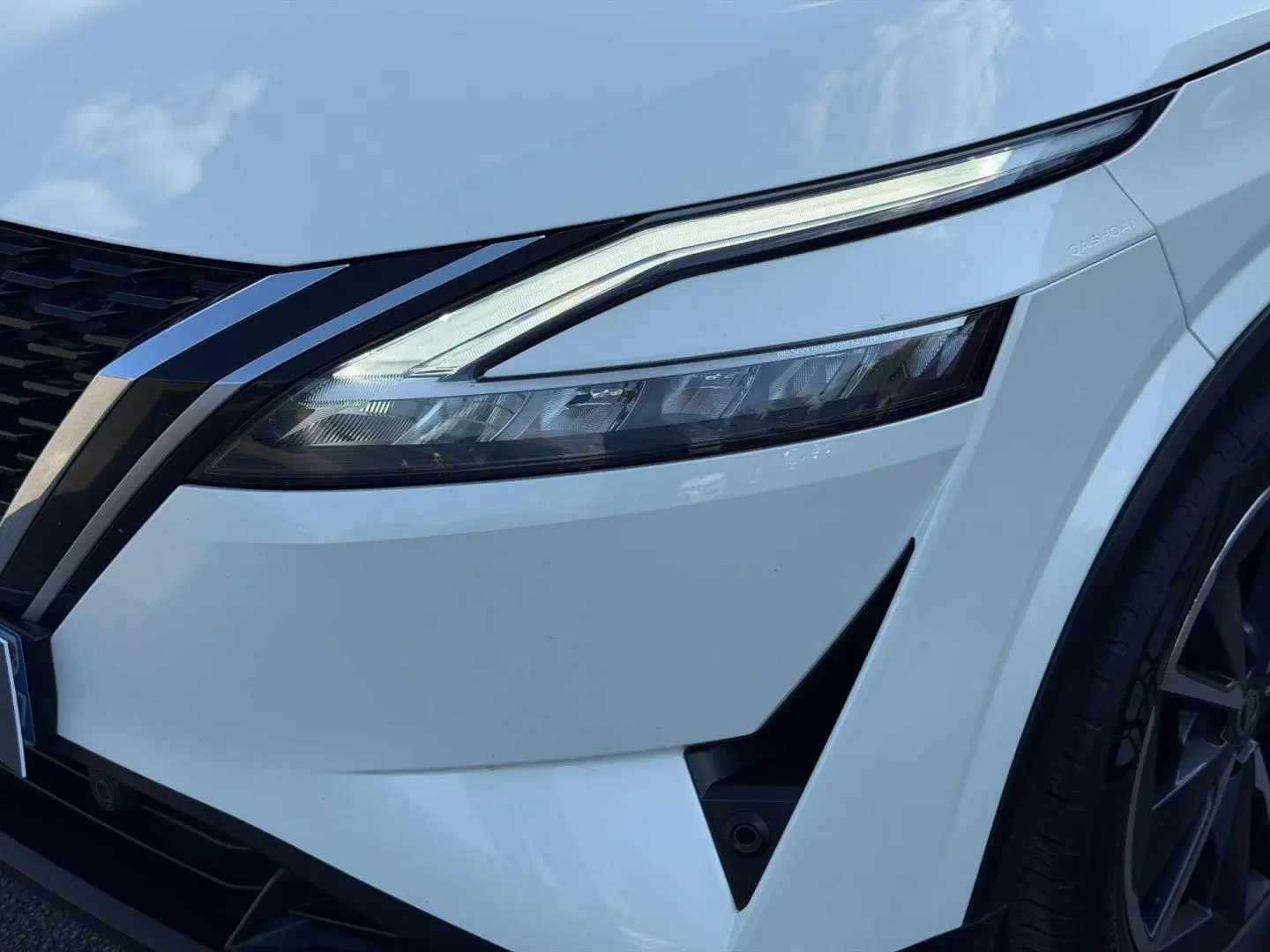 Gros plan sur l'avant droit blanc du Nissan Qashqai 2022, mettant en valeur le phare LED et la calandre noire.