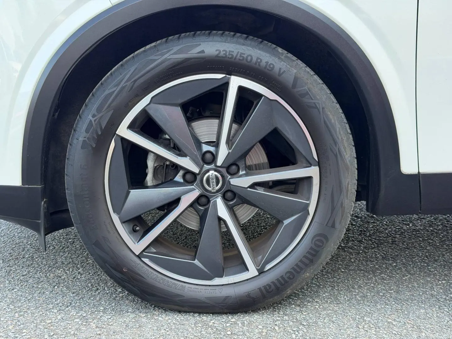 Gros plan sur la roue avant droite d’un Nissan Qashqai blanc avec jante alliage noire et argentée.