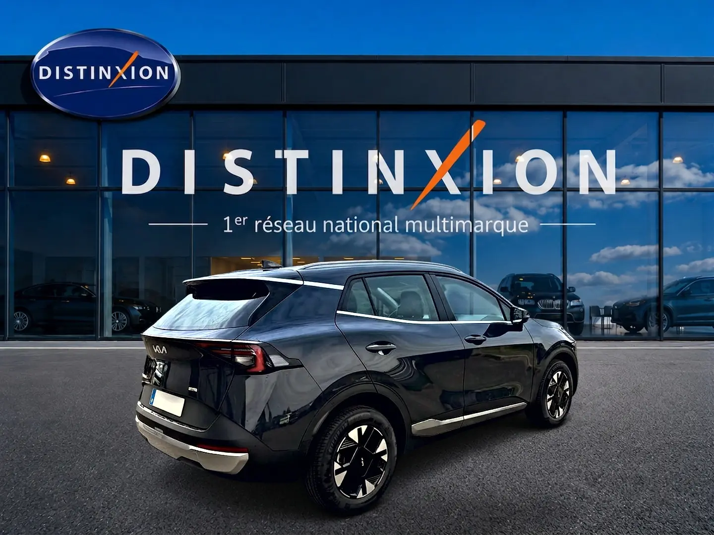 Vue 3/4 arrière droite d'un KIA SPORTAGE 1.6 hybride gris eclipse avec jantes alu et feux arrière LED, devant une vitrine Distinxion.