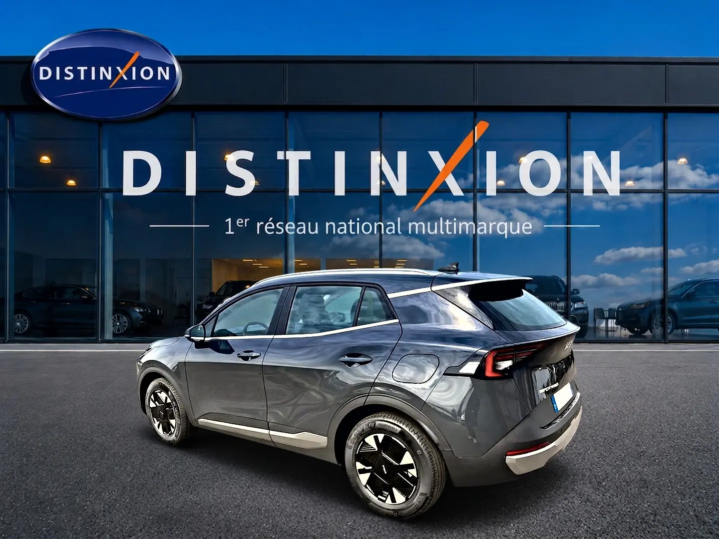 KIA SPORTAGE 1.6 hybride gris eclipse vu en 3/4 arrière droit devant un showroom Distinxion.