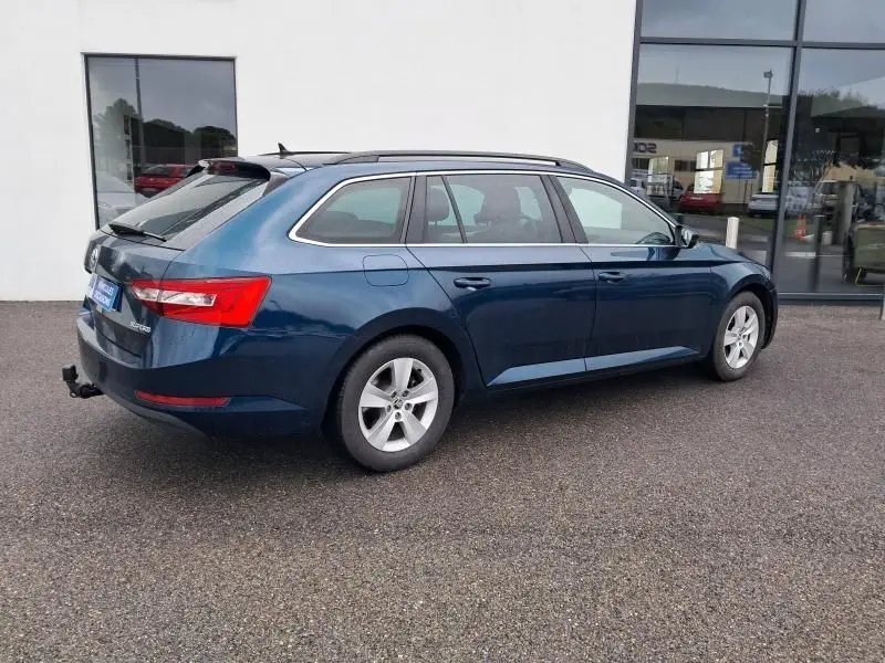 Skoda Superb Combi bleu métal 2018 vu de profil côté droit, avec barres de toit et attelage arrière visible.