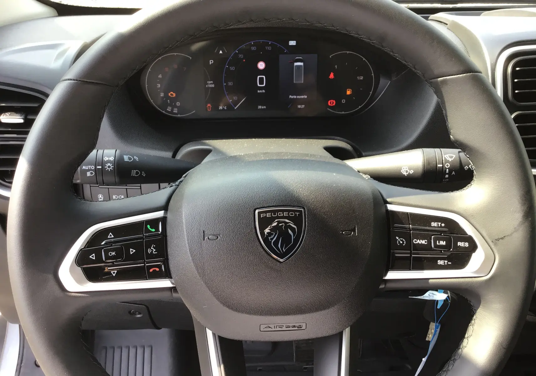 Vue rapprochée du volant noir de PEUGEOT Boxer Fourgon gris Artense, avec commandes intégrées et tableau de bord digital.