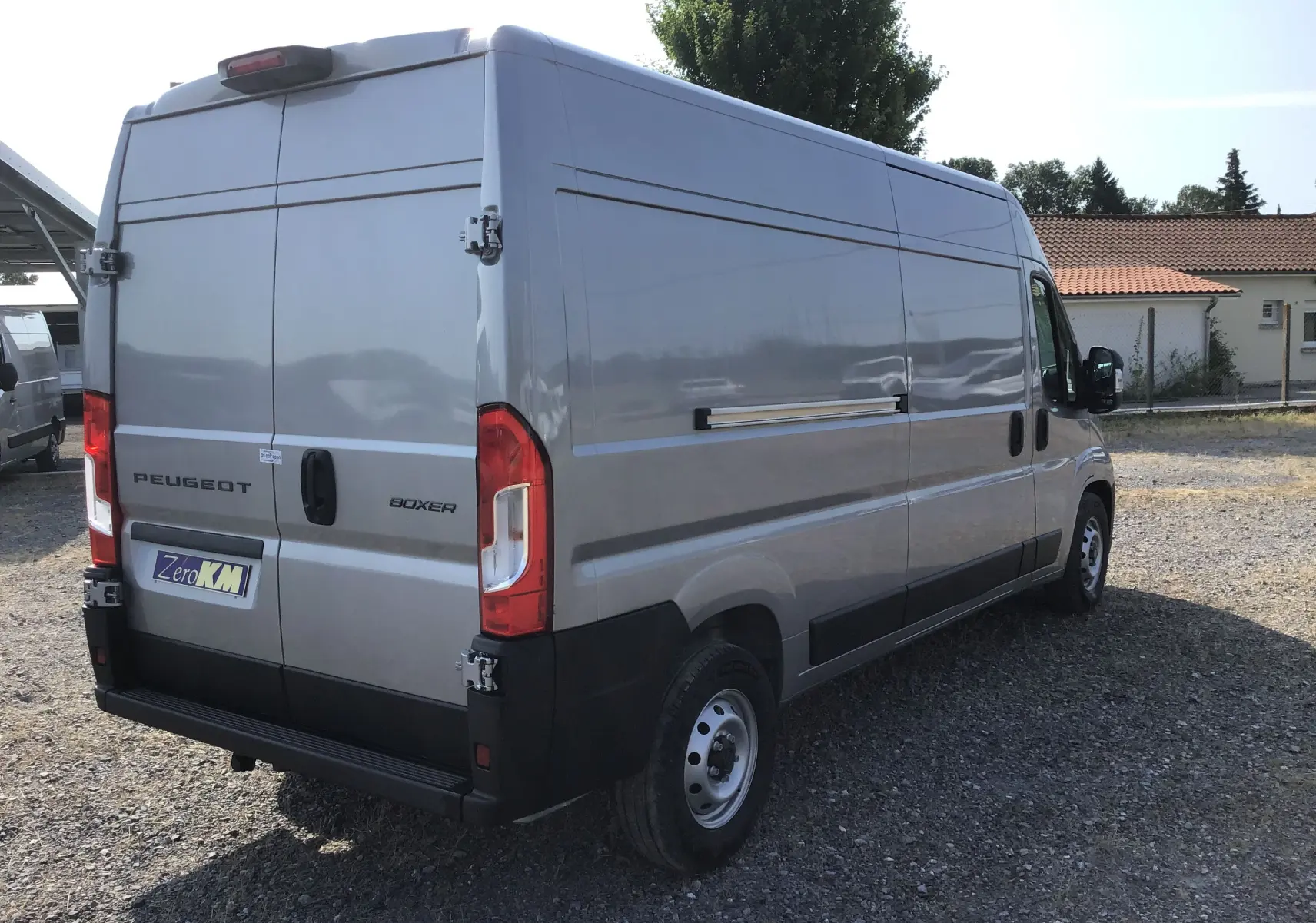 Vue 3/4 arrière droite d'un Peugeot Boxer Fourgon gris Artense stationné sur un sol gravillonné en extérieur.