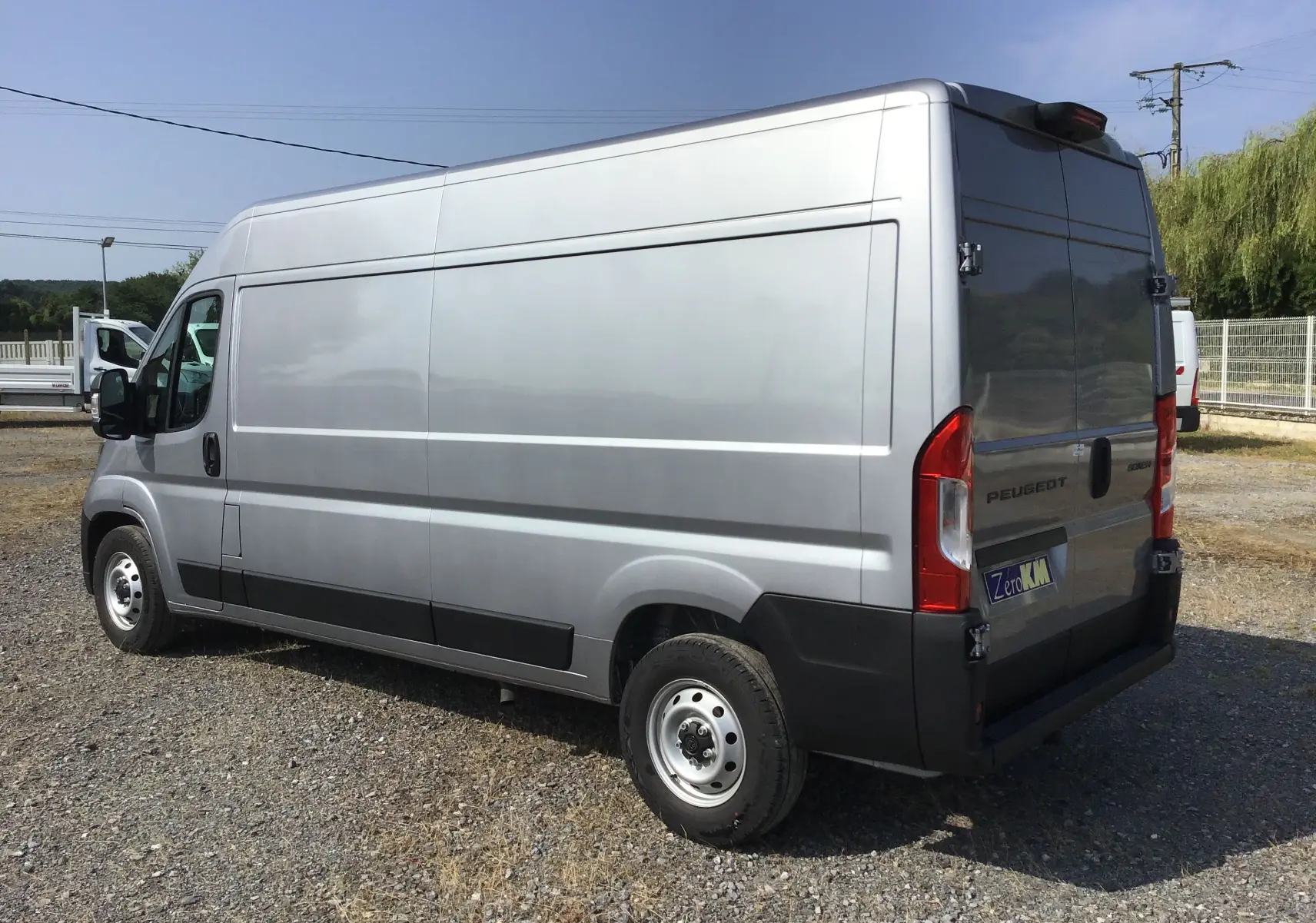 Vue 3/4 arrière droite d'un Peugeot Boxer Fourgon gris Artense avec portes arrière fermées sur un sol gravillonné.