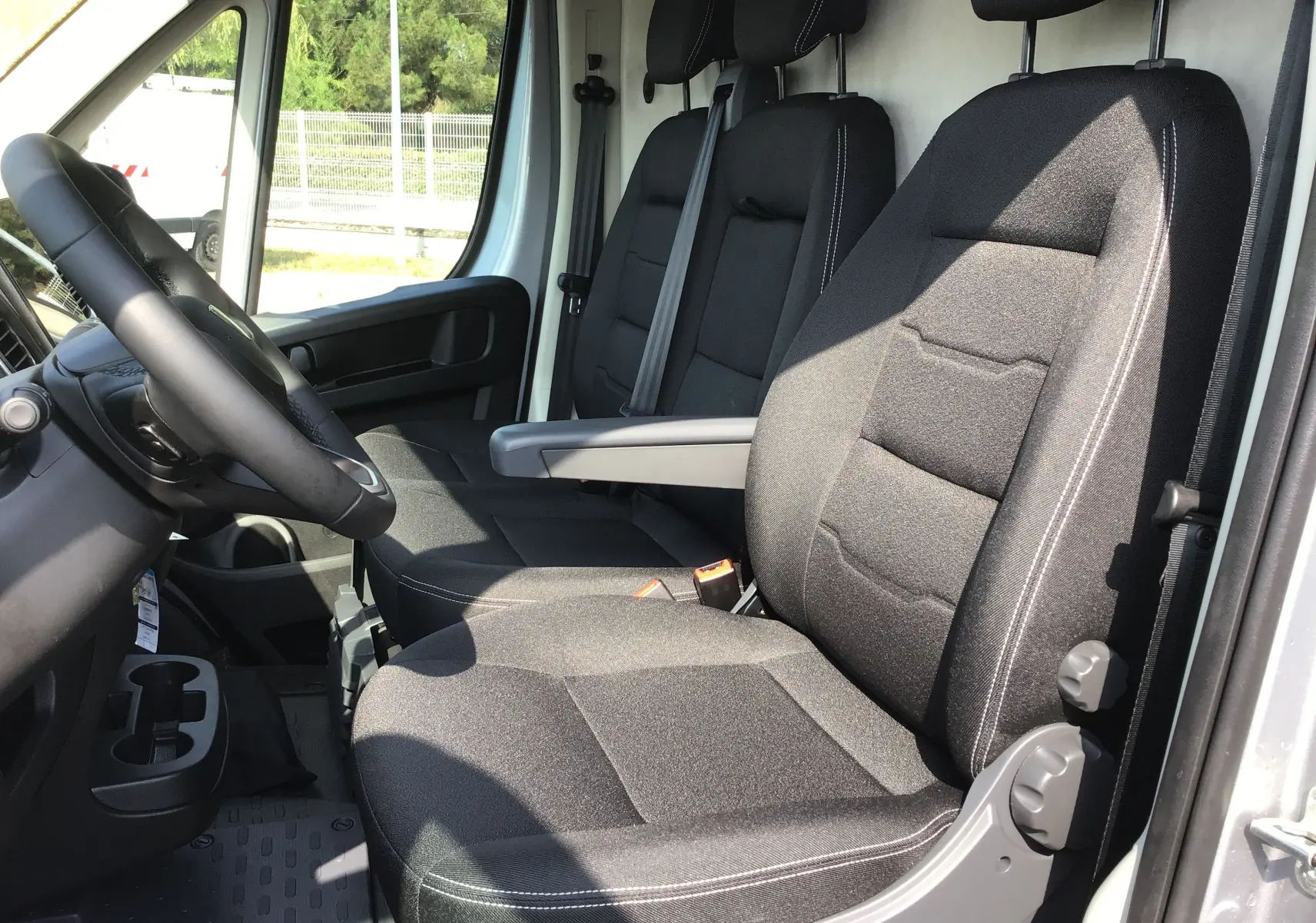 Intérieur du Peugeot Boxer Fourgon gris Artense, vue côté conducteur sur les sièges avant noirs avec accoudoir central.