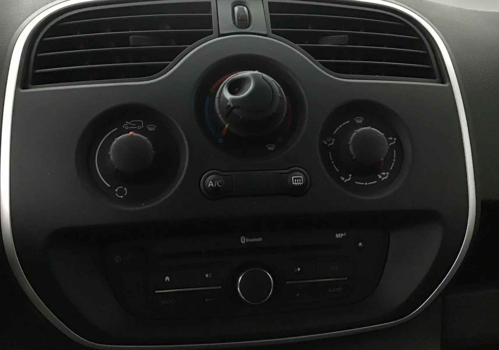 Tableau de bord noir du Renault Kangoo blanc 2021, avec commandes de climatisation et radio Bluetooth en gros plan.
