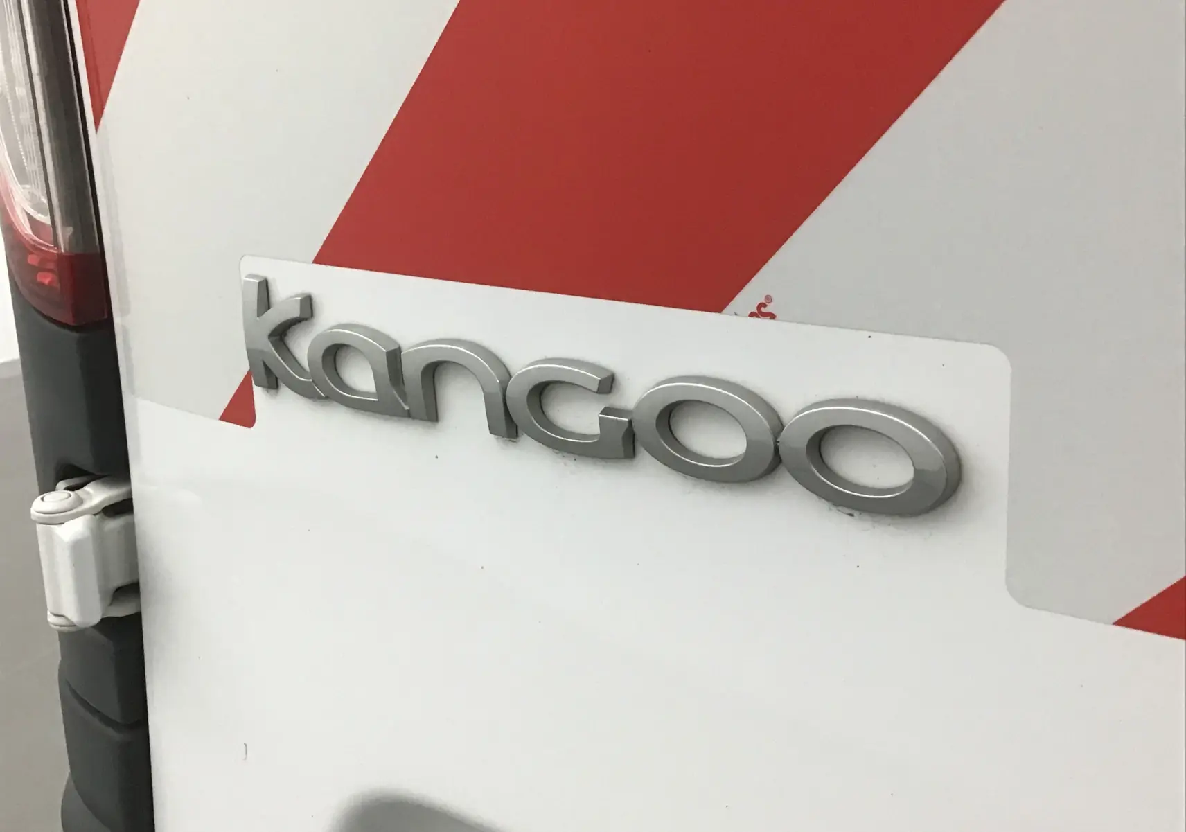 Gros plan sur l'arrière blanc d'un Renault Kangoo avec marquage du modèle et bandes rouges diagonales.