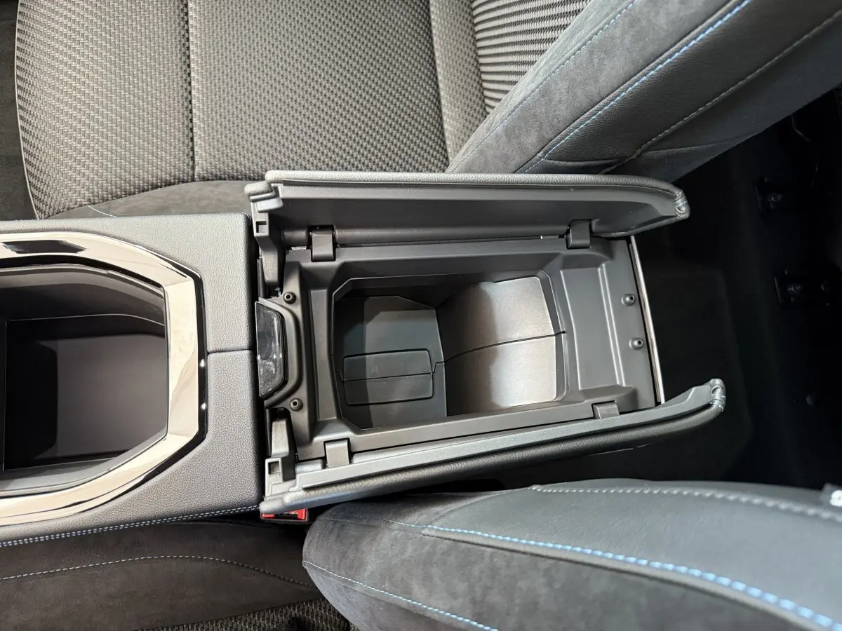 Vue plongeante sur la console centrale ouverte du Renault Espace gris foncé, montrant le rangement intérieur et les sièges en cuir noir avec surpiqûres bleues.