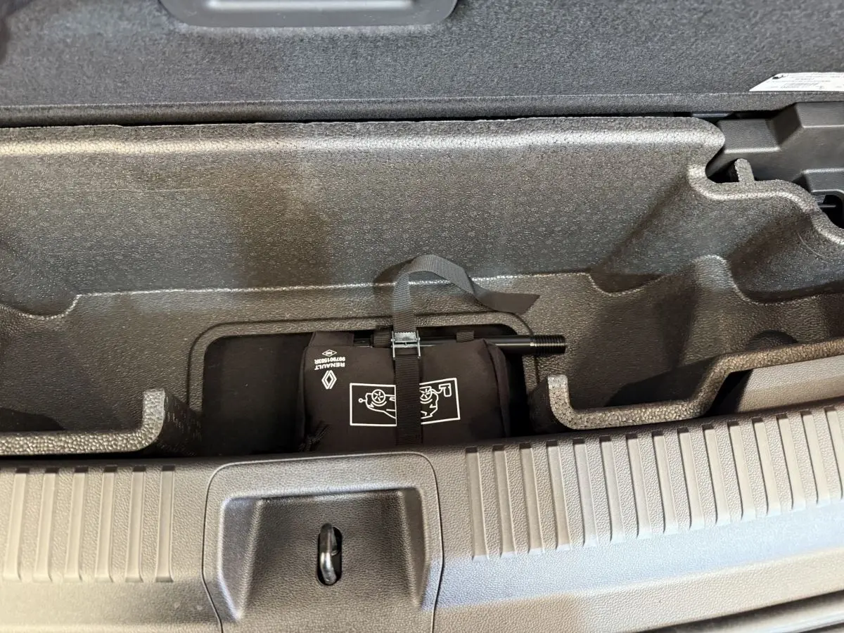 Compartiment de rangement sous le plancher du coffre du Renault Espace gris foncé, montrant l'outillage fixé par sangle.