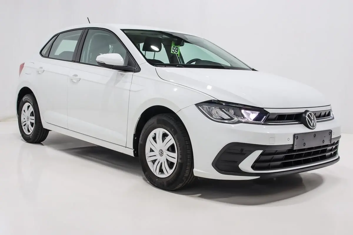 Volkswagen Polo blanche vue en 3/4 avant droit, avec phares allumés et jantes en acier à enjoliveurs.