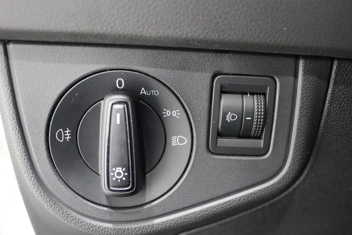 Gros plan sur la molette de réglage des phares et le variateur d'intensité lumineuse du tableau de bord d'une Volkswagen Polo blanche.