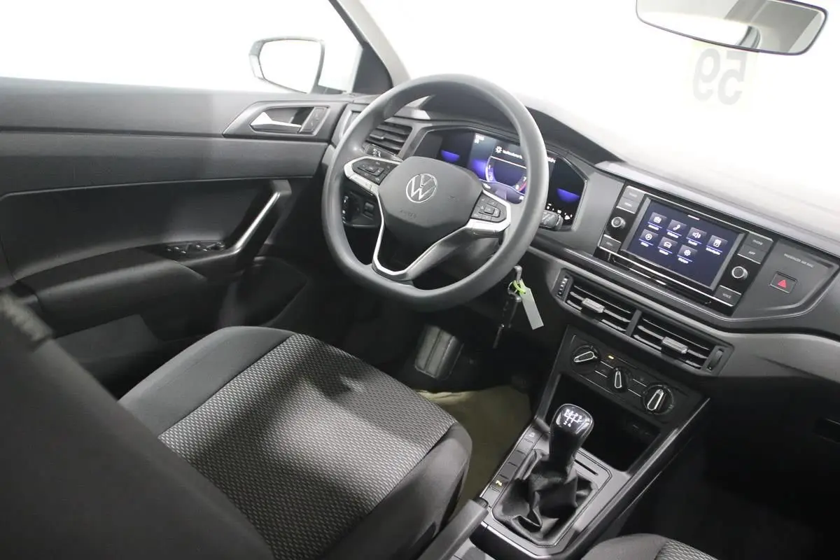 Vue intérieure côté conducteur de la Volkswagen Polo blanche 2022, avec volant multifonction et boîte manuelle visible.