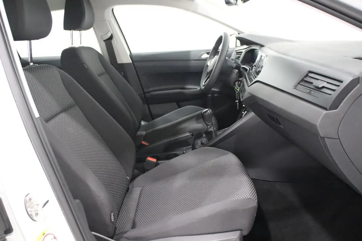 Vue intérieure côté gauche de la Volkswagen Polo blanche 2022, montrant les sièges tissu noirs et le tableau de bord.