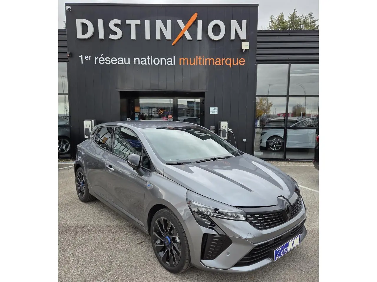 Renault Clio V hybride gris schiste métal vue 3/4 avant avec jantes alliage noires et calandre distinctive.
