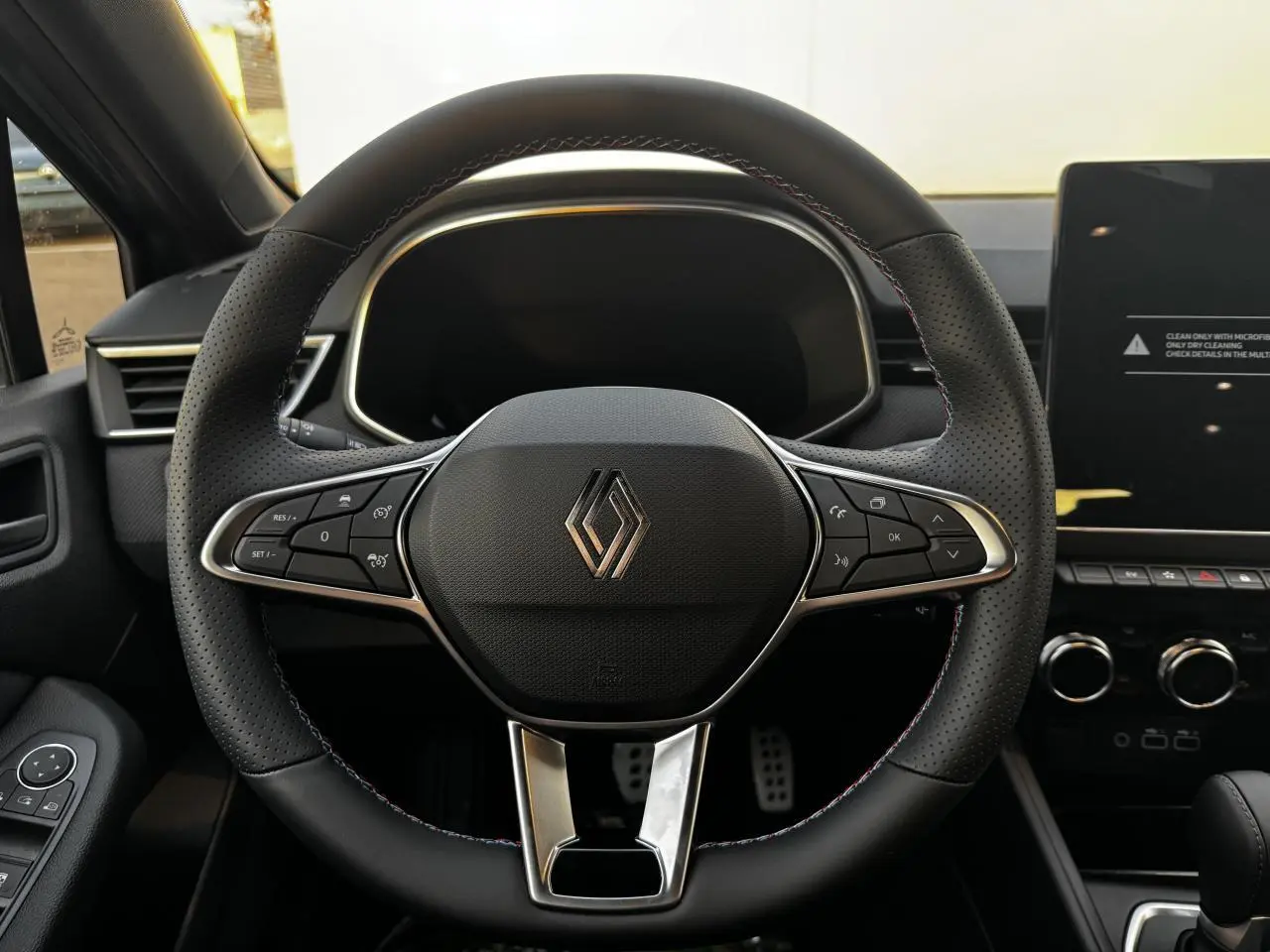 Volant perforé noir avec surpiqûres tricolores et logo Renault, tableau de bord et écran tactile à droite visibles