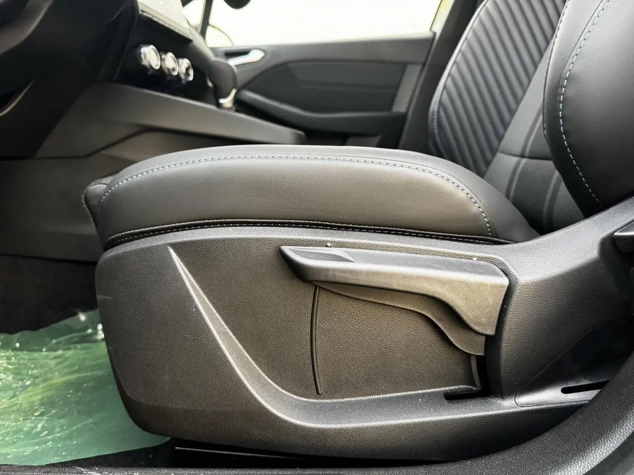 Gros plan sur l'accoudoir avant coulissant gris avec surpiqûres bleues dans l'habitacle de la Renault Clio V hybride.