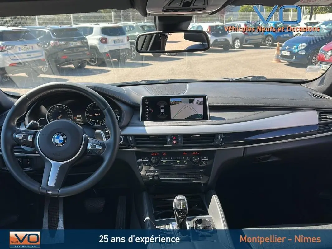 Intérieur BMW X6 F16 noir vu de face, volant sport cuir, écran GPS affichant caméra de recul, tableau de bord moderne.