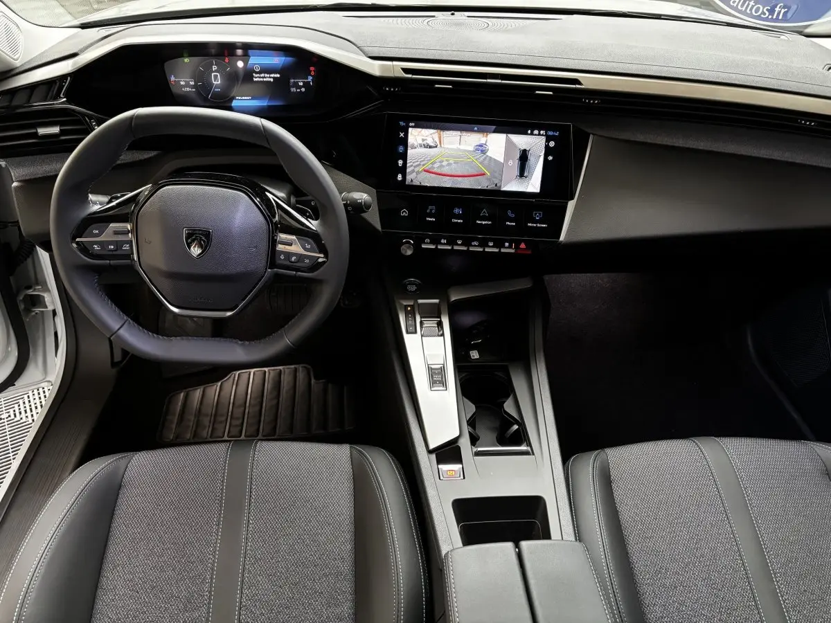 Vue intérieure avant de la Peugeot 308 Hybrid blanche, volant cuir multifonctions et écran tactile affichant la caméra de recul.