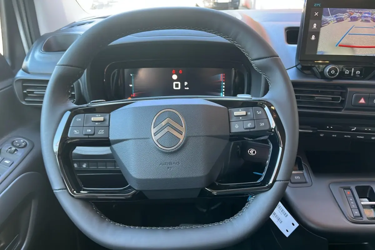 Vue intérieure centrée sur le volant cuir multifonctions du Citroën Berlingo 2025 avec écran tactile et tableau de bord numérique.